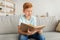 Cute redhead boy sitting at home, reading book