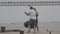 A cute romantic married couple dancing on the pier with a bridge on the background in overcast weather