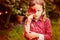 Cute sad child girl hiding behind red autumn leaf in the garden