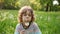 A cute schoolboy with curly hair is blowing a dandelion against the backdrop of a summer green glade. Dynamic video