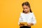 cute schoolchild with backpack holding book isolated on orange .