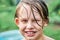 Cute schooler with wet blond hair stands against lush trees