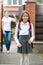 Cute schoolgirl standing in front of house. Mother waving standing in doorway and waving to her