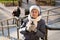 Cute senior woman in city drinks coffee with herself in winter coat and warm hat, scarf and knitted gloves in sunny winter weather