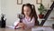 A cute serious girl puts a tripod gadget for her phone on the table and prepares for the lesson by spreading a textbook