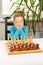 Cute seven year old child boy playing chess at home on a white wooden table. Selective focus