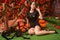 Cute sexy pin up girl in black outfit relax by sitting on the grass with background of autumn leaves. black hair witch