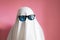 Cute sheet ghost costume with sunglasses on a pink background. Halloween party carnival concept