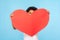 Cute shy adorable little boy peeking out from big red paper heart, unrecognizable child holding symbol of love