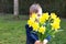 Cute shy little boy in blue vest holding and giving bouquet of bright yellow daffodils flowers hiding his face behind it.