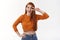 Cute and silly ginger girl in orange cropped top, jeans, hold hand on hip, make peace or victory sign near eye and