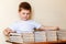 A cute six-year-old boy sits at a Desk and puts books on stacks