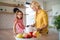 A cute small girl with mother indoors in kitchen at home.