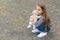 Cute small kid play with toy dog sitting on pebble pavement outdoors, playing, copy space