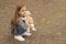 Cute small kid play with toy dog sitting on pebble pavement outdoors, playing, copy space