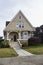 Cute small Victorian house with shingle siding and bay window and flowers in the yard