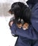 Cute smallblack scared dog sitting on man& x27;s hands in snowy winter park