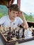 Cute, smart, boy in shirt sits in the classroom and plays chess on the chessboard. Training, lesson, hobby, education concept.