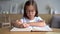 Cute smart primary school child girl reading book at home table