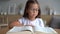 Cute smart primary school child girl reading book at home table