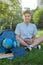 Cute, smart, young boy in blue shirt sits on the grass next to his school backpack, globe, chalkboard, workbooks. Education