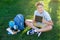 Cute, smart, young boy in blue shirt sits on the grass next to his school backpack, globe, chalkboard, workbooks. Education