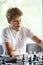 Cute, smart, young boy in white shirt plays chess on the chessboard in the classroom. Education, hobby, training