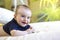 Cute Smiling baby boy with blue T-shirt in white sunny bedroom with green plant.