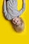Cute smiling blond boy hanging upside down on yellow background. Vertical frame