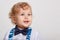 Cute smiling blonde baby kid boy in white shirt with bow tie and suspenders, looking aside over white background, having curious