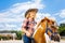 Cute smiling cowboy girl leading little beautiful pony