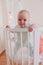 Cute smiling european baby stands in an oval white crib.