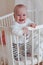 Cute smiling european baby stands in an oval white crib.