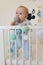 Cute smiling european baby stands in a white canopy bed and plays with balls.