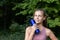 Cute smiling girl athlete with a sports bottle of water in nature in the forest or park on a blurred background of green trees and