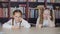 Cute smiling girls holding pens and sitting at table in library