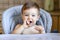 Cute smiling hungry little boy holding spoon and playing with it waiting for food, looking at camera