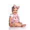 Cute smiling infant baby girl toddler in polka-dot dress and headband with bow sits on the white floor