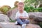 Cute smiling little Asian 1 year old toddler baby boy child with eyes closed practices yoga and meditating outdoors on nature