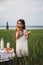 Cute smiling little girl in white dress eating bagel with milk in green field, summertime