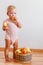 Cute smiling one-year-old girl stands barefoot and eats ripe large pears at home on white background