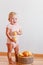 Cute smiling one-year-old girl stands barefoot and eats ripe large pears at home on white background