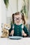 Cute smiling preschool age girl in round big glasses hold in hands fork and a spoon, learning to use cutlery