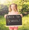 Cute smiling schoolgirl standing with blackboard outdoors sunny