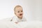 Cute smilling 9 month boy in white bodysuite on white background. Laughing infant kid under blanket. Copy space.