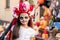 Cute spooky girl with painted face standing against young woman in dress and hat