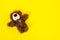 Cute stuffed toy in shape of fluffy brown smiling bear with patches lies on yellow background with its paws spread out