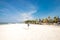 Cute stylish girl in blue dress standing on the amazing beach with wite sand, holding smartphone in her hands. She has