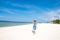 Cute stylish girl in blue dress standing on the amazing beach with wite sand, holding smartphone in her hands. She has