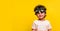 Cute stylish kid in pilot glasses isolated on yellow background. Child dreams to be a pilot and playing with plane